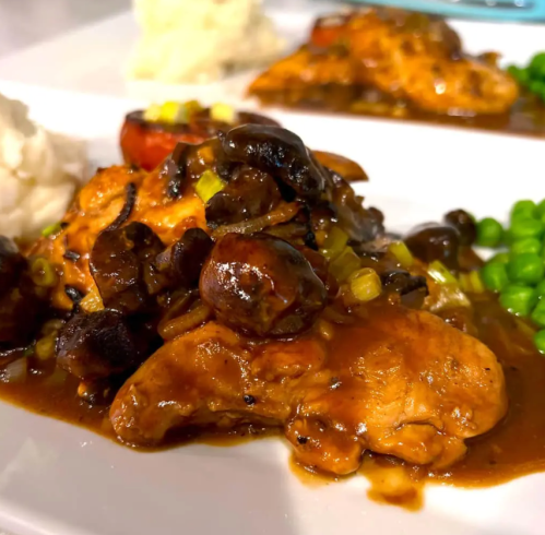 A plate of chicken in mushroom sauce, served with mashed potatoes and green peas.