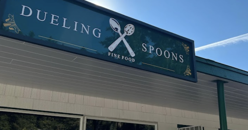 Sign for "Dueling Spoons Fine Food" featuring two crossed spoons against a blue sky.