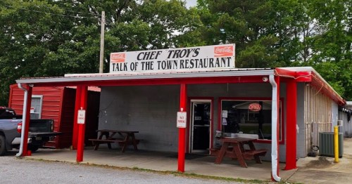 Exterior of Chef Troy's Talk of the Town Restaurant, featuring a red and white sign and picnic tables outside.