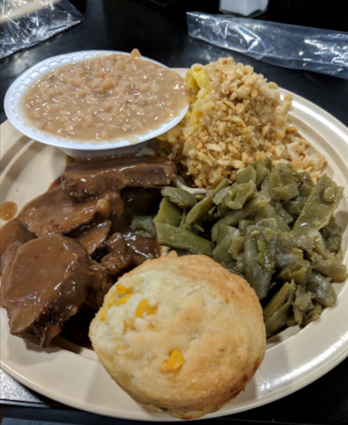A plate of food featuring beef with gravy, green beans, rice, baked beans, and a cornbread muffin.