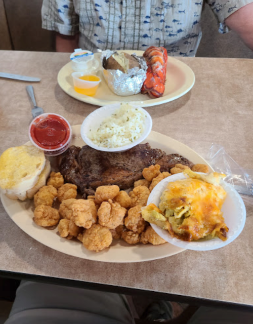 A plate of fried shrimp, steak, rice, baked potato, and a side of cheesy casserole, with a person in the background.