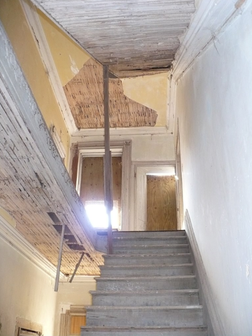 A worn staircase leads to a dimly lit upper level, with peeling walls and exposed wood.