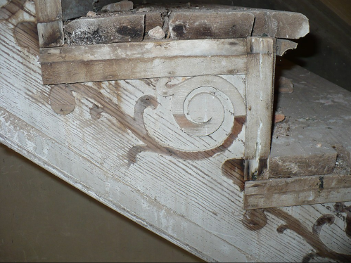 Close-up of a worn wooden staircase with decorative carvings and peeling paint, showing signs of age and neglect.