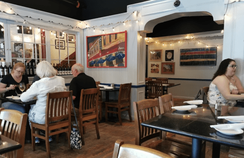 A cozy restaurant interior with wooden tables, string lights, and patrons dining and chatting.