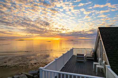 Sunset over calm waters, with a deck and clouds reflecting vibrant colors in the sky.