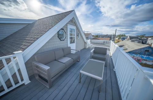 Rooftop deck with modern furniture, including a sofa and table, overlooking a scenic view under a partly cloudy sky.