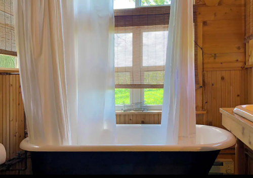 A cozy bathroom featuring a clawfoot tub, sheer white curtains, and natural light from a window with bamboo shades.