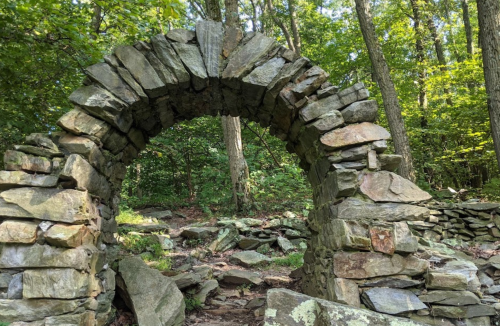 Stone archway surrounded by lush greenery and trees in a forested area.