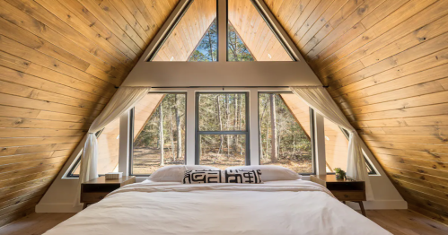 Cozy A-frame bedroom with large windows, wooden walls, and a serene forest view.
