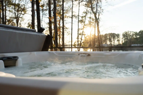 A hot tub with bubbling water, surrounded by trees, with a sunset reflecting on the water in the background.