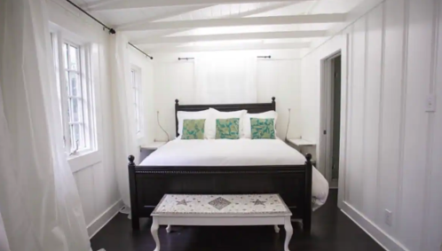 Cozy bedroom with a large bed, white walls, and green accent pillows, featuring natural light and simple decor.