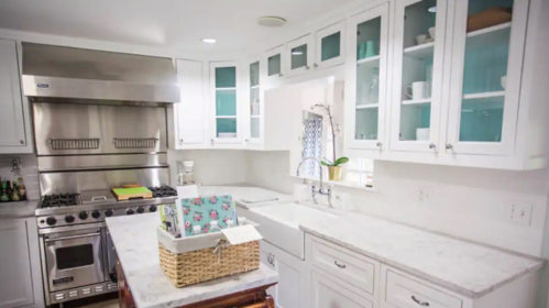 Bright kitchen with white cabinets, stainless steel appliances, and a marble countertop, featuring a sink and decorative basket.