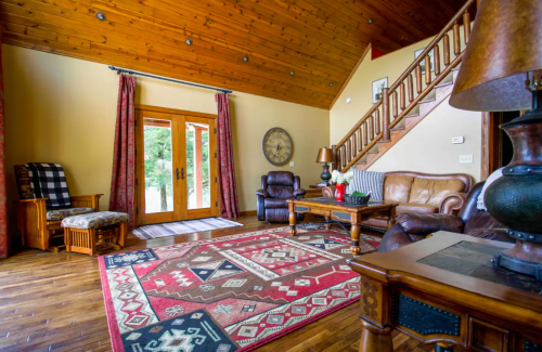 Cozy living room with wooden ceiling, plush furniture, a patterned rug, and large windows letting in natural light.