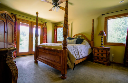 Cozy bedroom with a wooden four-poster bed, dresser, and large windows letting in natural light.