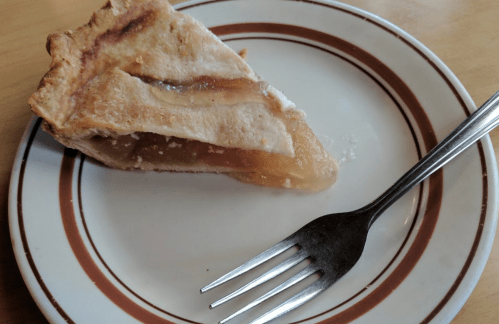A slice of apple pie on a plate with a fork beside it. The crust is golden brown and flaky.