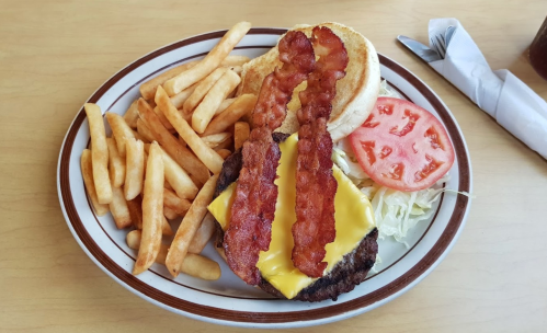 A cheeseburger with bacon, lettuce, and tomato, served with a side of French fries on a plate.