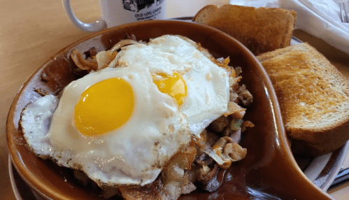 A bowl of breakfast featuring two sunny-side-up eggs, sautéed vegetables, and two slices of toast on the side.