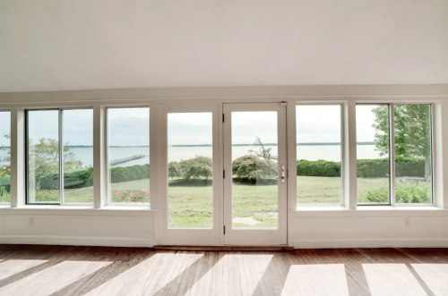 Bright room with large windows overlooking a serene waterfront view and green landscape.