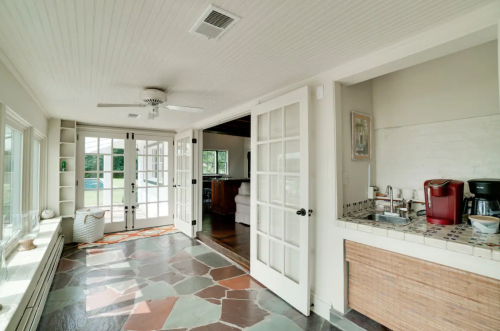 Bright sunroom with stone flooring, French doors, and a small kitchenette featuring a coffee maker and woven storage.
