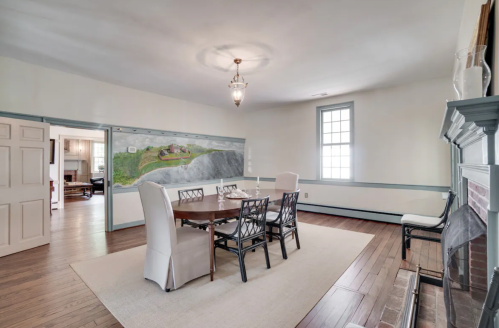 A dining room with a round table, four chairs, and a mural on the wall, featuring a scenic landscape.