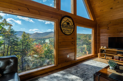 Cozy wooden interior with large windows showcasing a scenic mountain view and a "Bearloga" sign on the wall.