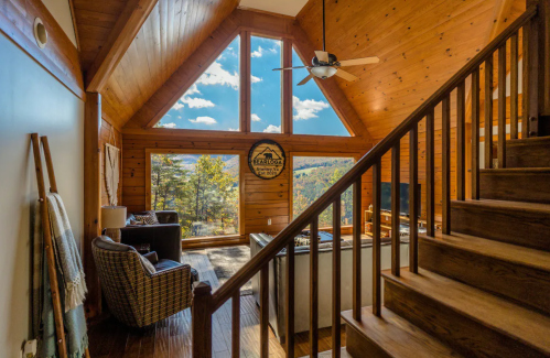Cozy wooden cabin interior with large windows, a staircase, and a living area featuring comfortable seating and scenic views.