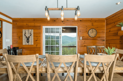 Cozy dining area with wooden chairs, a rustic table, and a view of mountains through sliding glass doors.