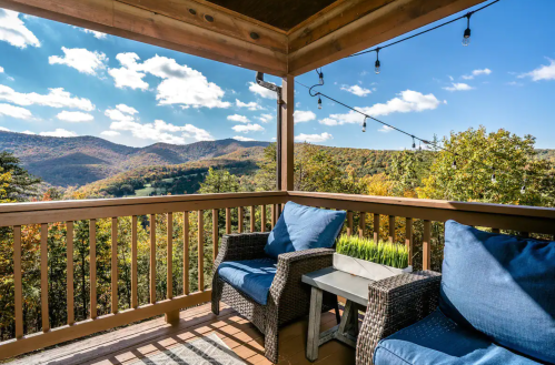Cozy balcony with blue chairs, a small table, and a scenic view of mountains and autumn foliage under a bright sky.
