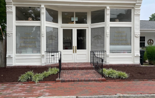A wellness center with large windows displaying services like yoga, massages, and holistic healing, featuring brick steps.