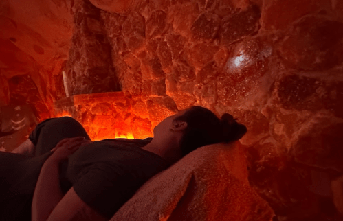 A person relaxes against a textured salt wall in a softly lit, warm-toned environment.