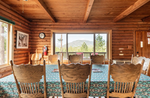 A rustic wooden dining area with a patterned tablecloth, featuring a view of mountains through large windows.