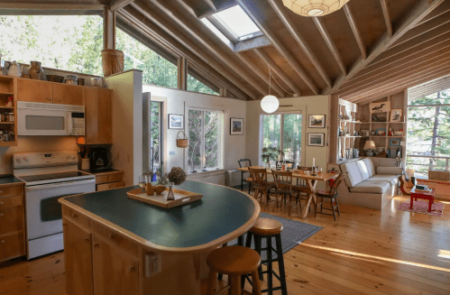 Cozy, modern kitchen and living area with wooden beams, large windows, and a dining table in a bright, airy space.