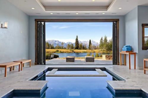 A luxurious indoor pool with a view of mountains and trees through large open doors.