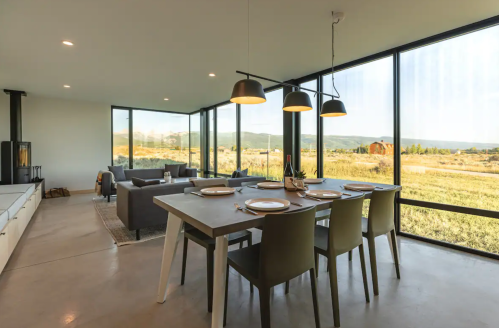 Modern dining area with a large table, stylish chairs, and panoramic windows showcasing a scenic outdoor view.