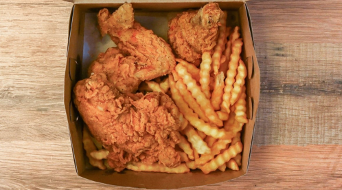 A takeout box filled with crispy fried chicken pieces and crinkle-cut fries on a wooden surface.