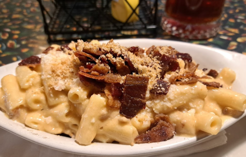 Creamy macaroni and cheese topped with crispy bacon and breadcrumbs, served in a white dish.