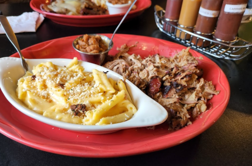 A red plate with creamy macaroni and cheese, pulled pork, and a small cup of baked beans.