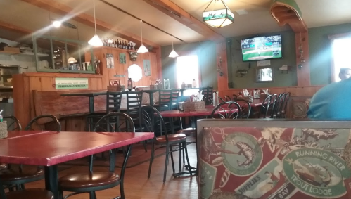 A cozy restaurant interior with wooden decor, empty tables, and a TV showing a sports game in the background.