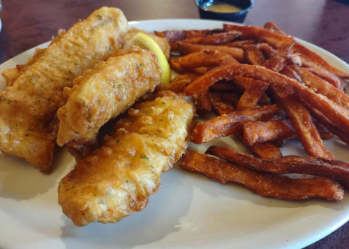 A plate of crispy fried fish fillets with a lemon wedge, served alongside golden sweet potato fries.
