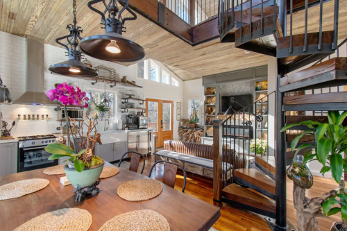 A stylish open-concept living space with a dining table, spiral staircase, and modern kitchen, featuring natural light and decor.