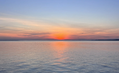 A serene sunset over calm waters, with soft pastel colors reflecting on the surface.