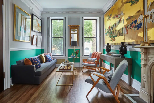 A stylish living room with a green accent wall, modern furniture, and artwork, featuring a cozy sofa and decorative elements.