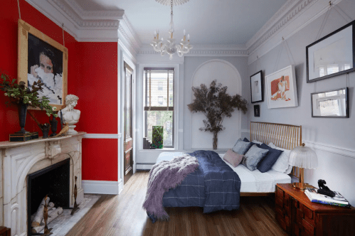 Cozy bedroom with a red accent wall, elegant decor, a fireplace, and a large window letting in natural light.