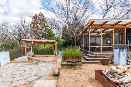 A serene outdoor space featuring a stone pathway, wooden structure, and a screened porch surrounded by greenery.