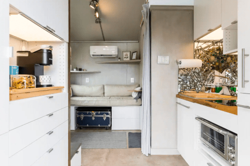 A modern, compact kitchen and living area with a sofa, storage, and a small dining space in a stylish interior.
