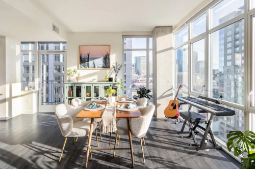 Bright, modern apartment with a dining area, large windows, city views, and a music setup in the corner.