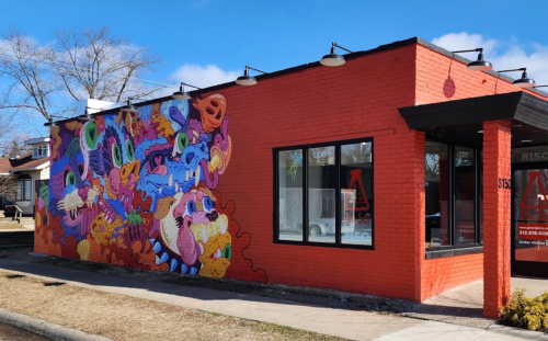Colorful mural on a red brick building, featuring abstract shapes and playful designs against a clear blue sky.