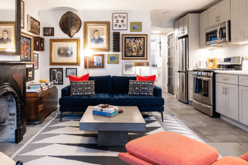 A cozy living room with a blue sofa, colorful artwork on the walls, and a modern coffee table in a stylish kitchen setting.