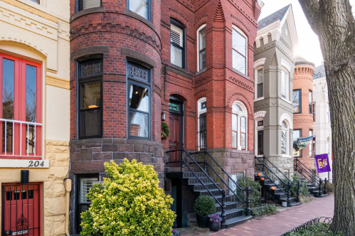 Colorful historic townhouses with unique architectural details and steps leading to the entrances, lined along a brick sidewalk.