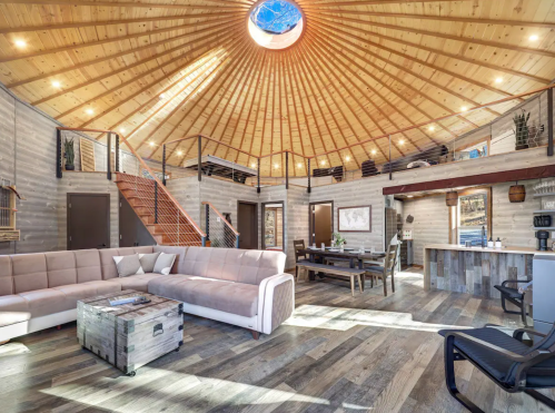 A spacious, modern interior of a round cabin with wooden beams, a skylight, and cozy furniture.